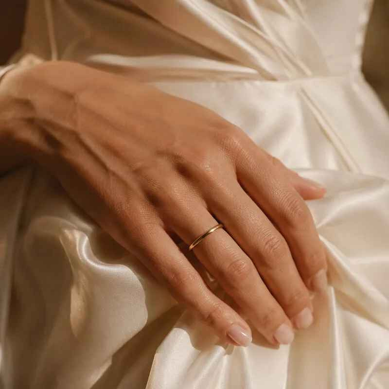 Hand mit schmalem Ring am Satinkleid