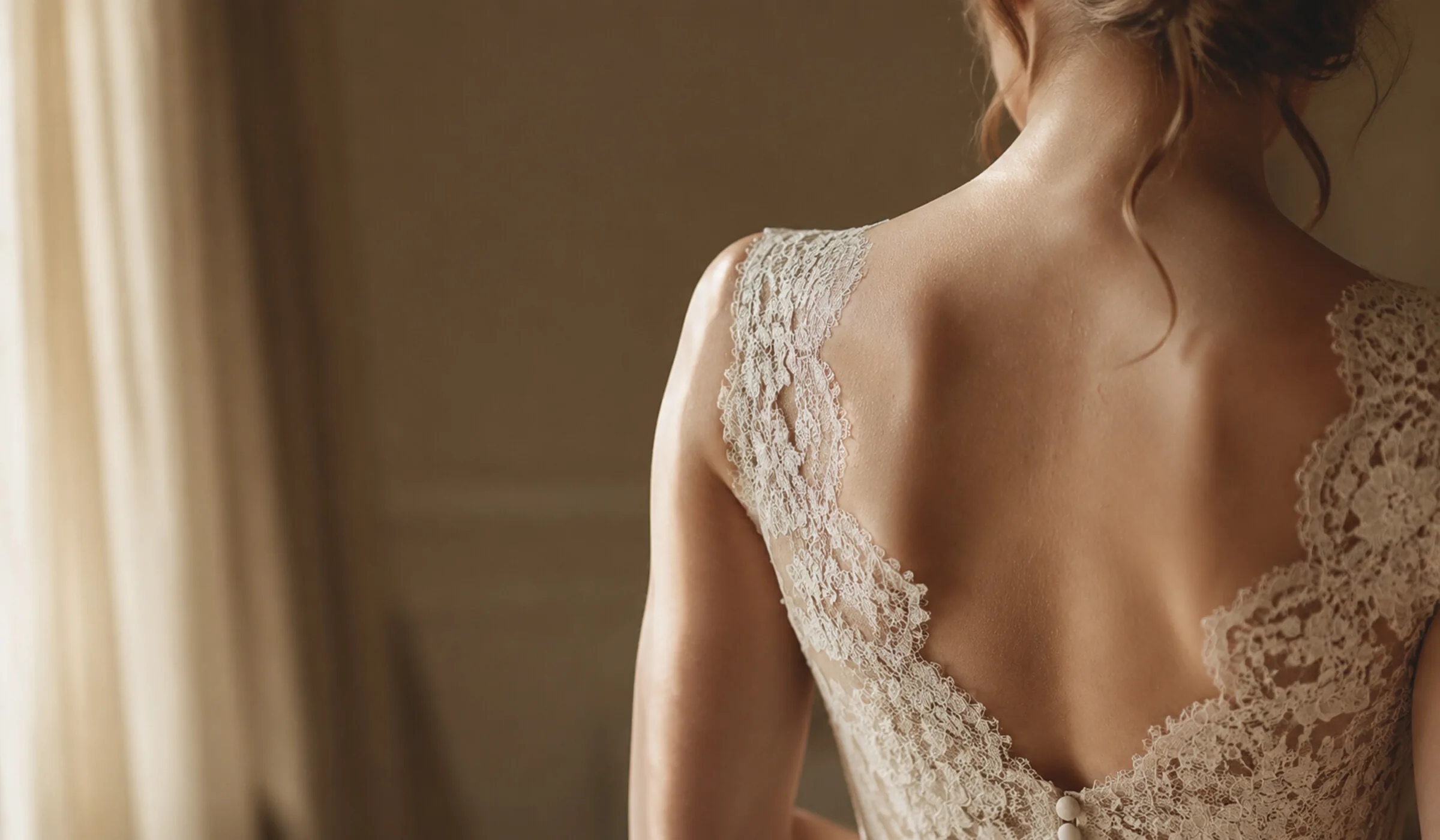 Rückenausschnitt einer Braut in einem cremefarbenen Spitzenkleid